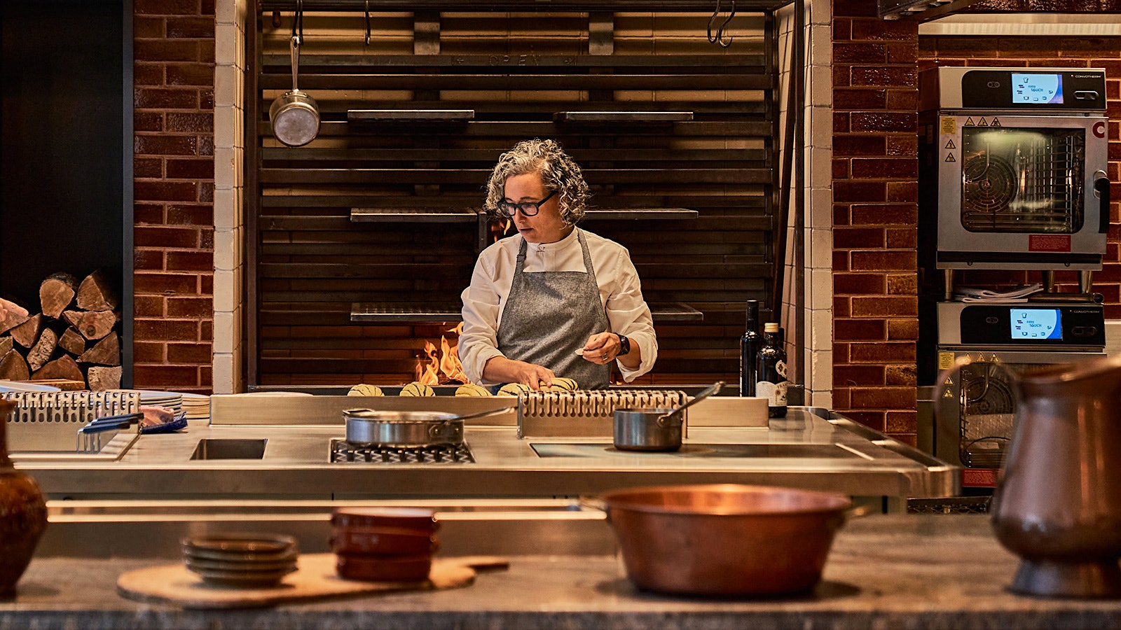 Hillary Sterling cooking in the kitchen at Ci Siamo, with the wood-fired oven in back of her.